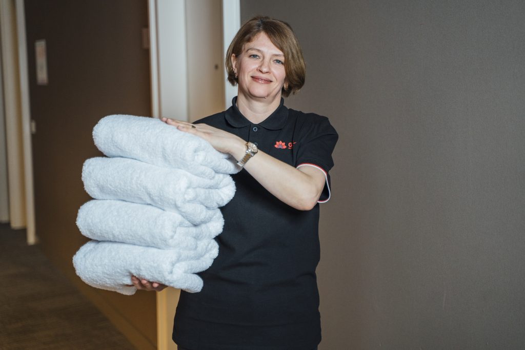 GRG Reinigungskraft bringt frische Handtücher in Hotelzimmer.